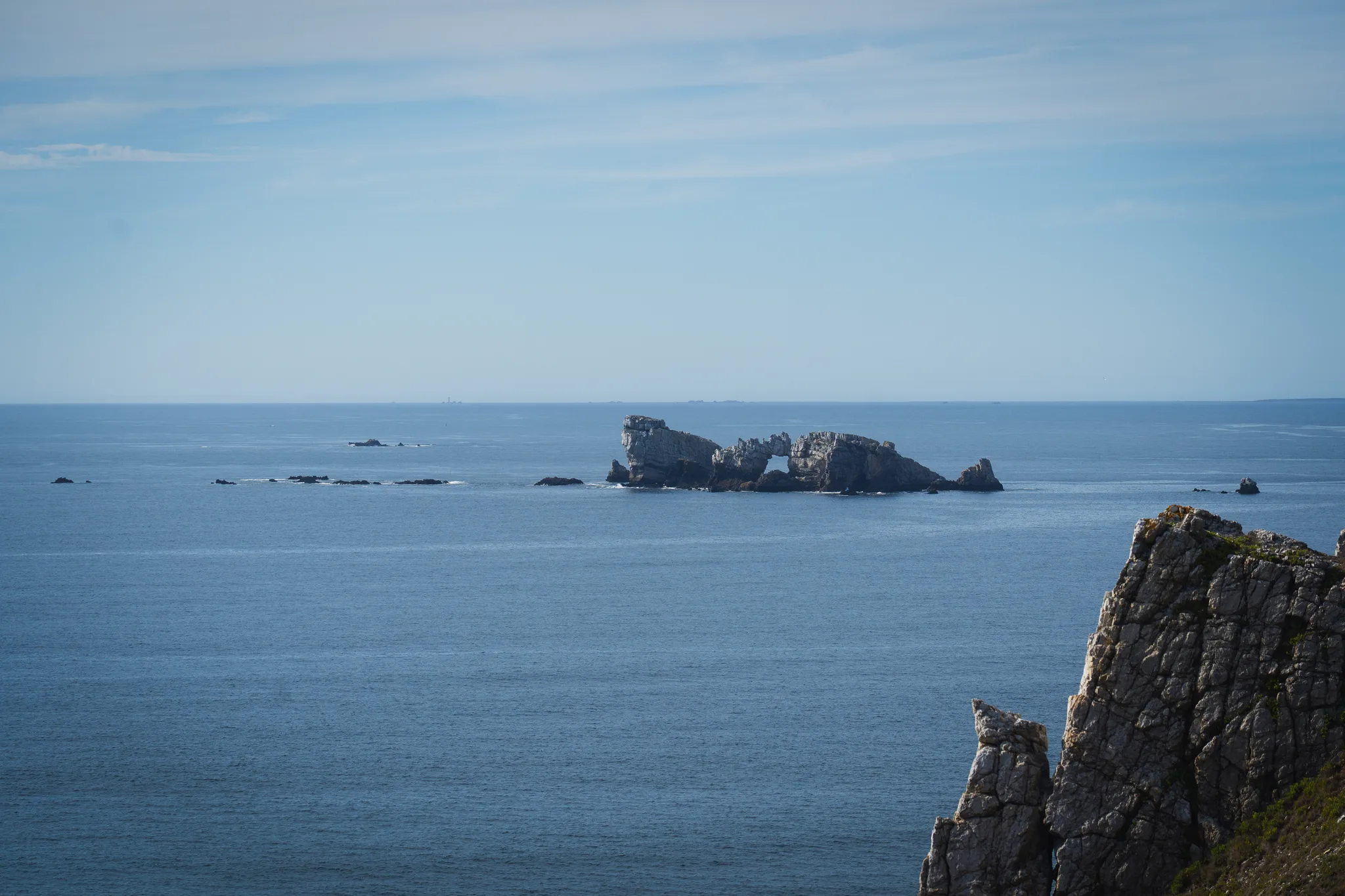 The Château de Dinan rock and its arch seen from the cliffs over a calm blue sea