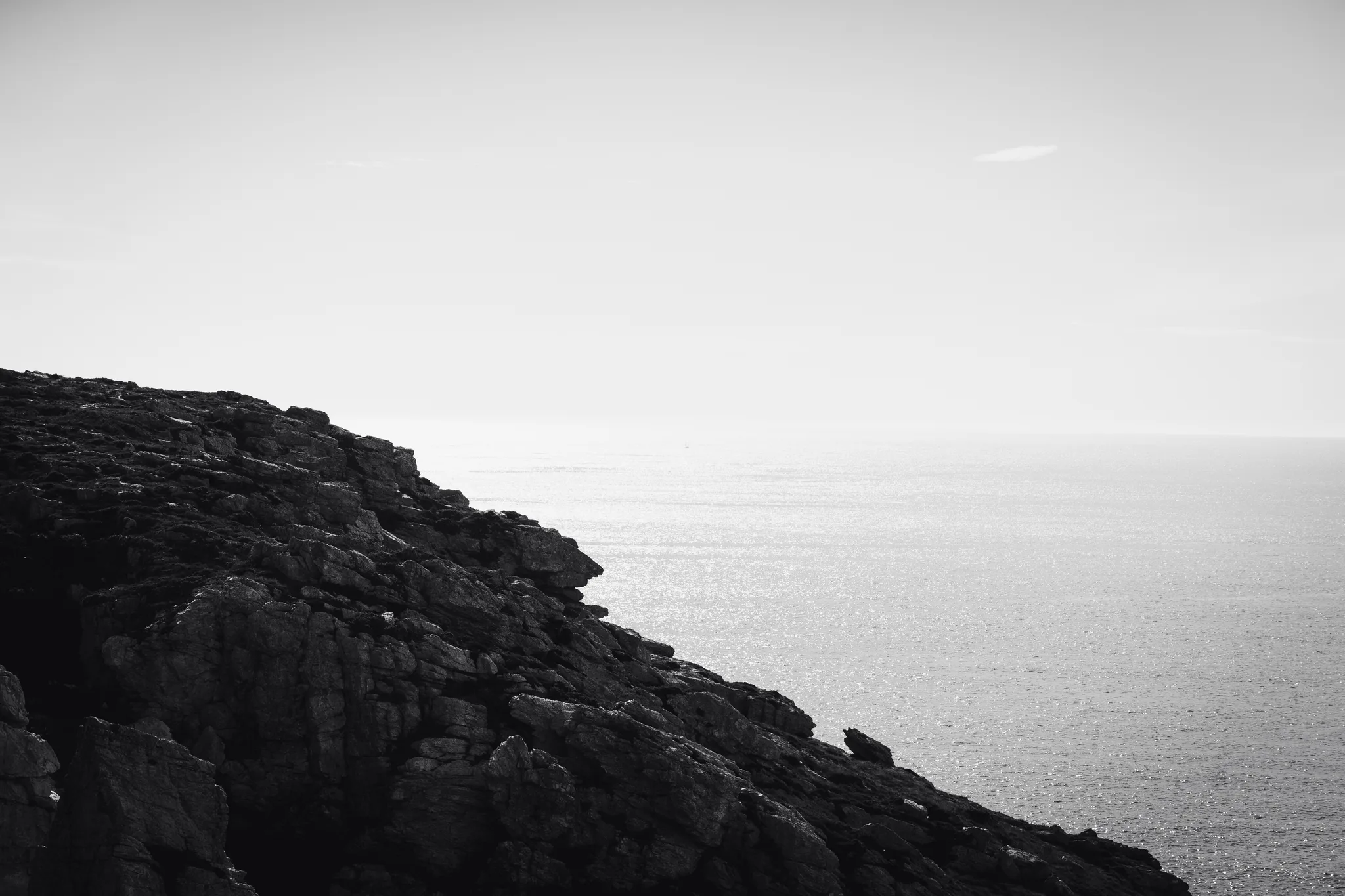 Dark rocky cliff silhouetted against a silver sea, black and white