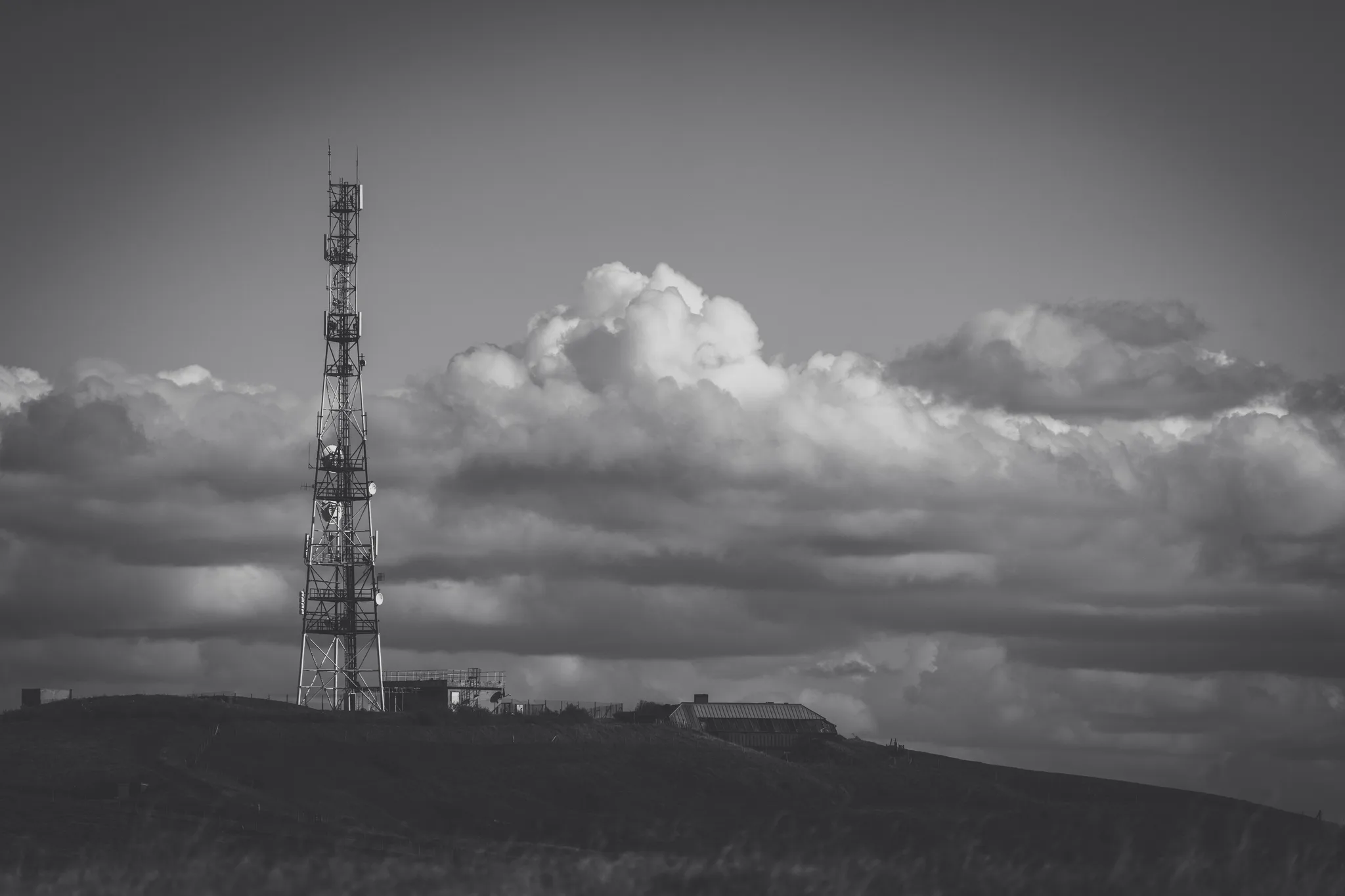 Radio mast and buildings on the hill under big clouds, black and white