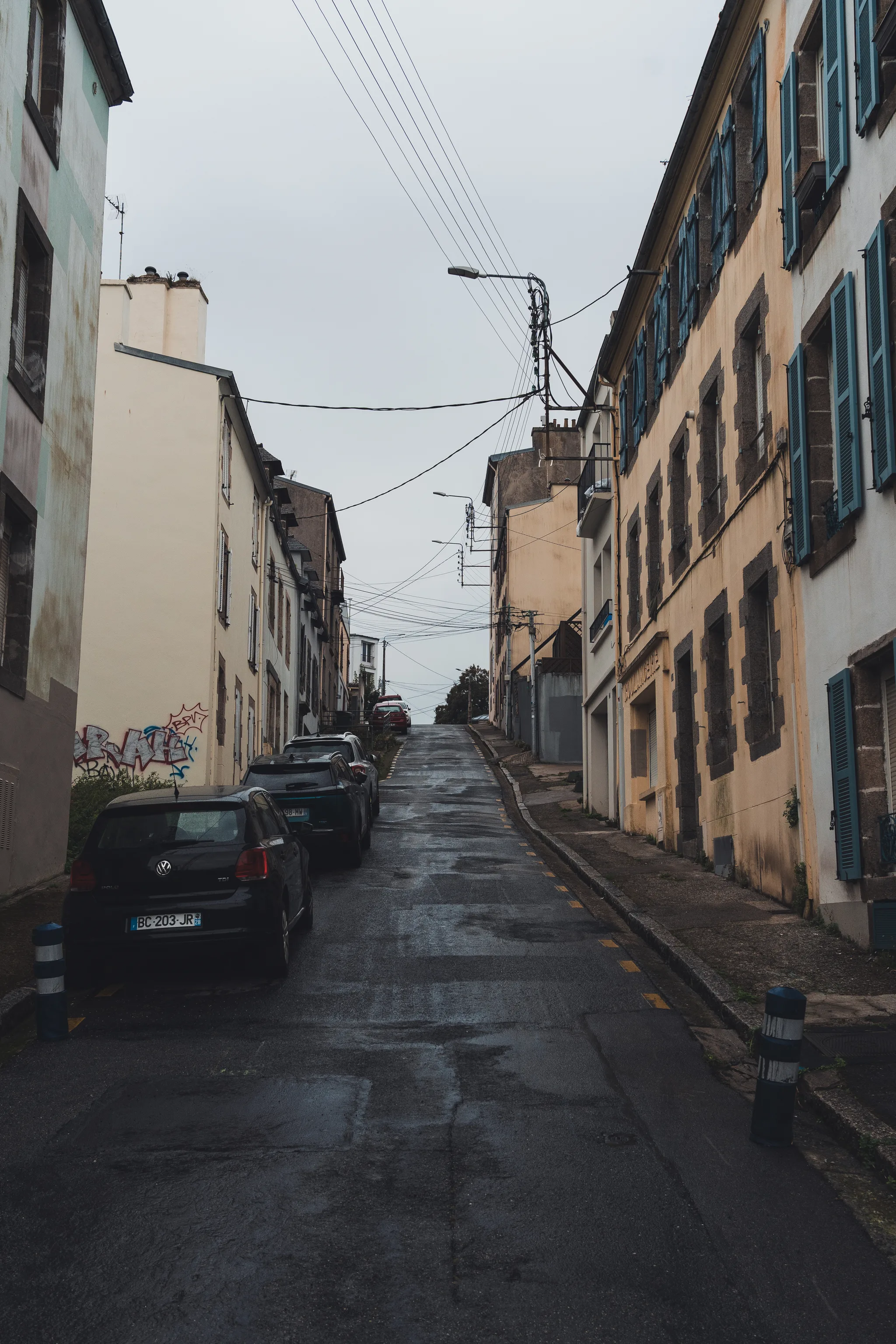 Steep narrow street with blue shutters and parked cars