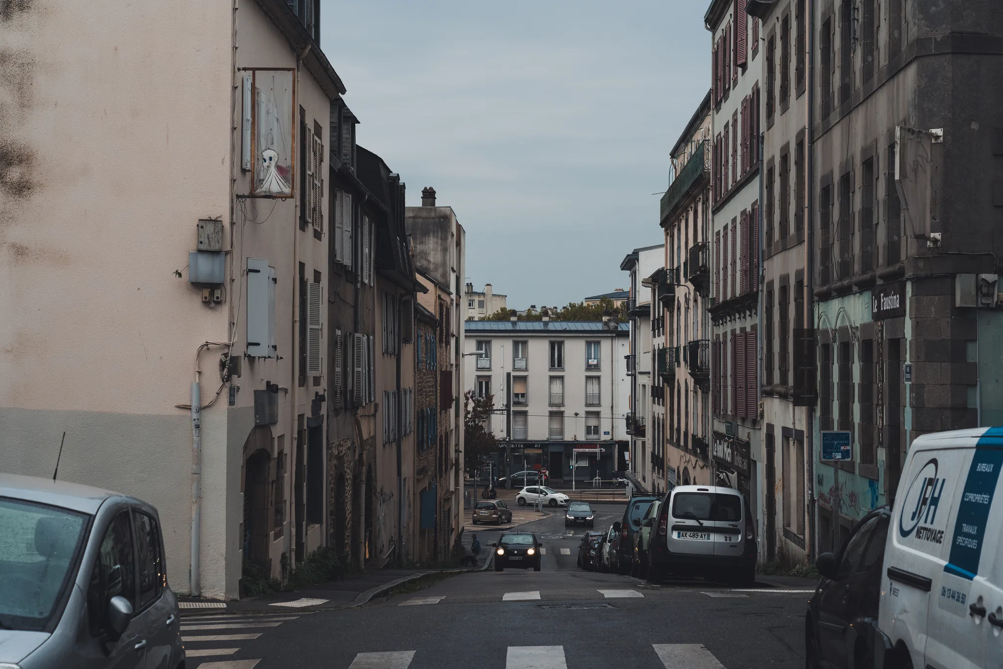 Sloping street of old houses down to an intersection, a white van in the foreground