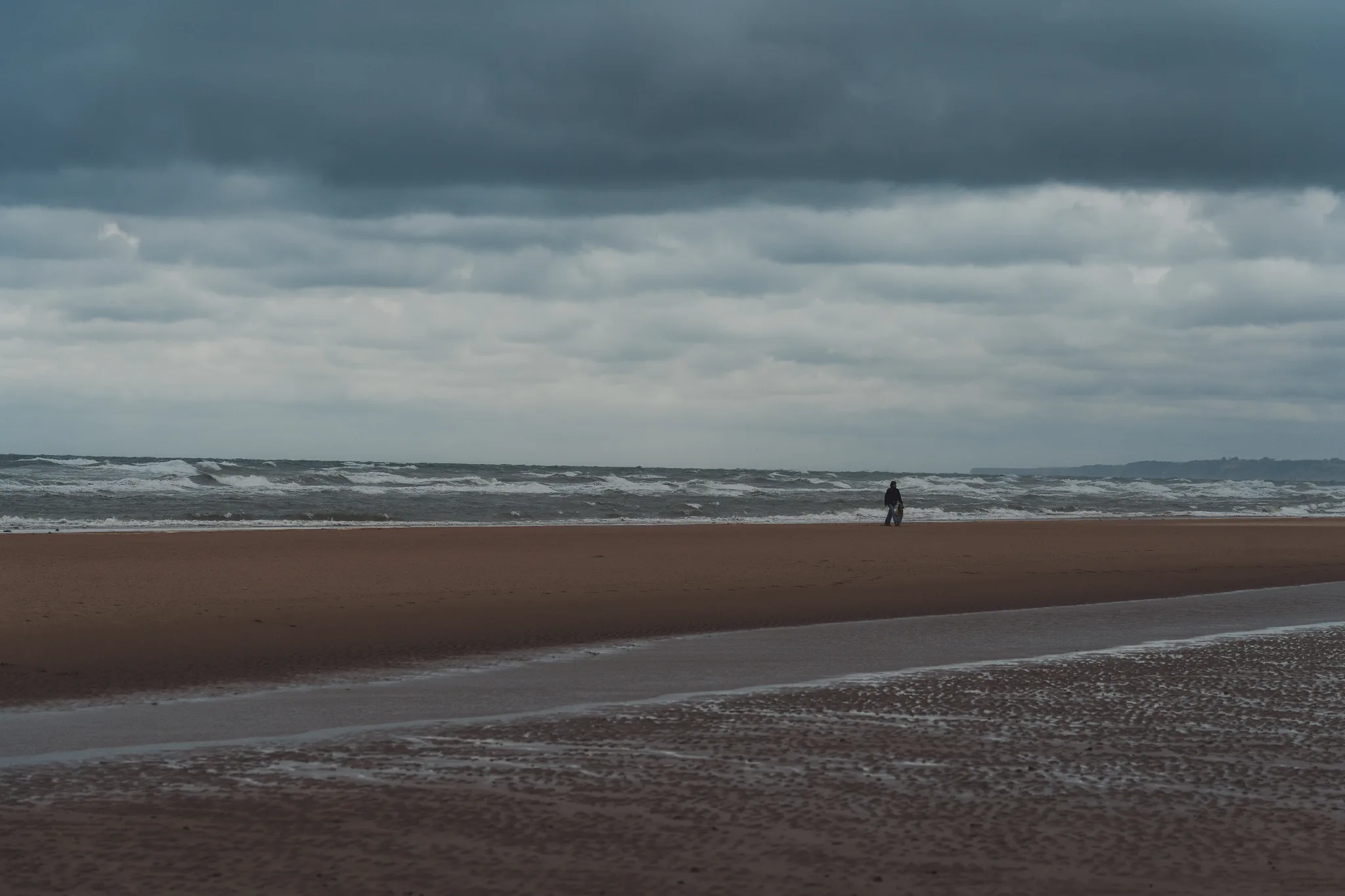 A lone figure on a wide beach by rough surf