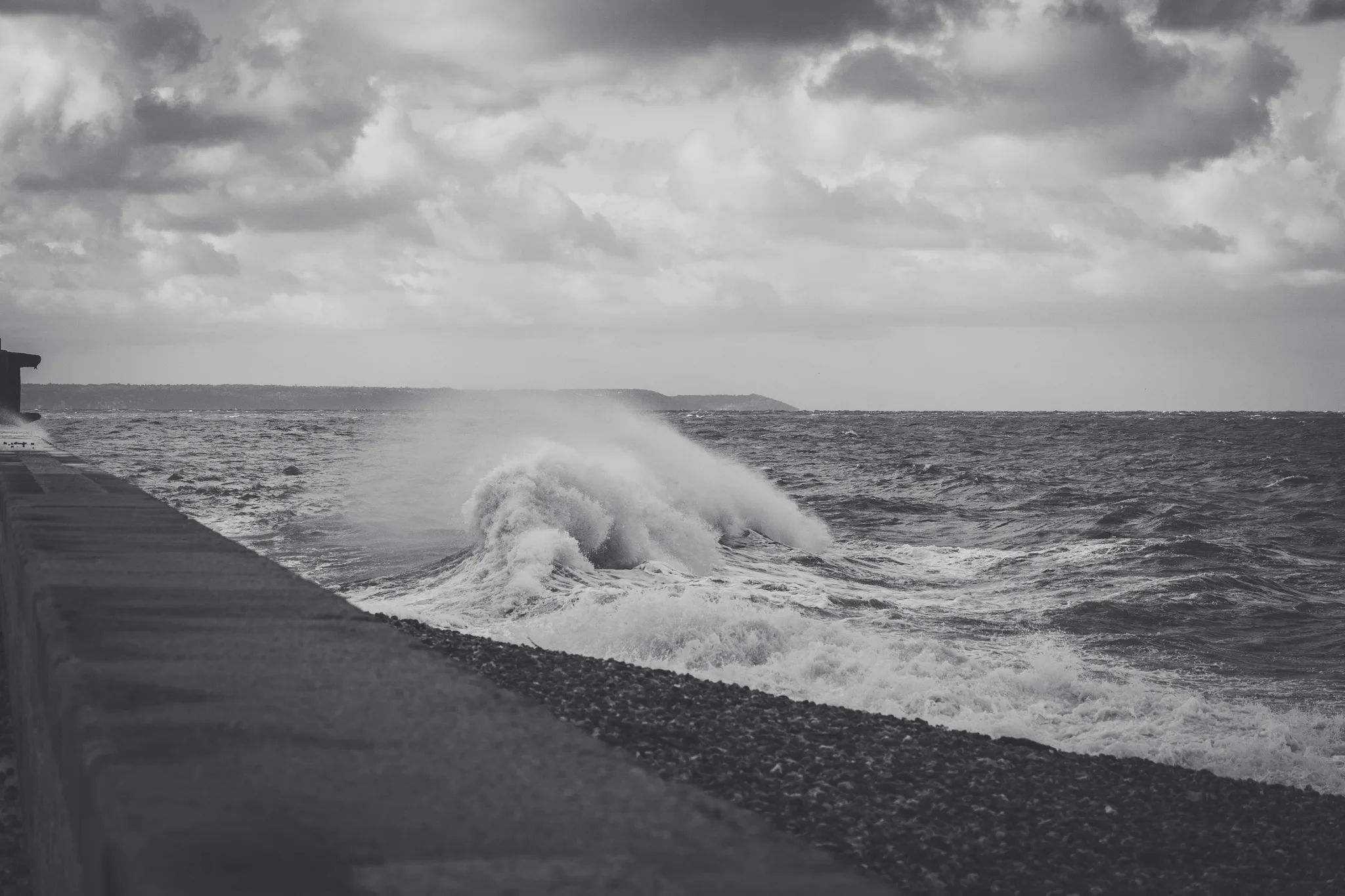 A large wave breaking against a sea wall, black and white