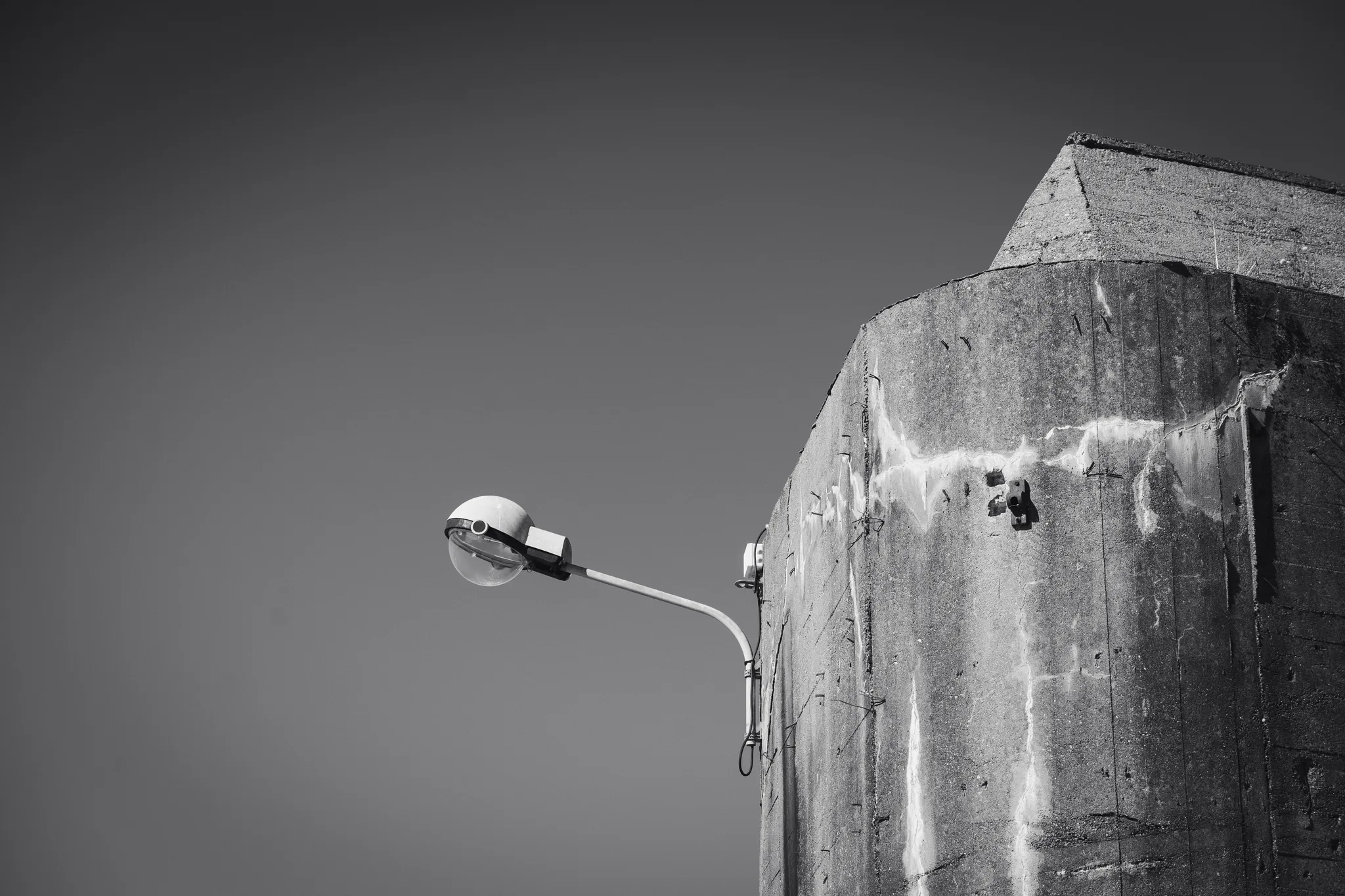 Street lamp in front of a weathered concrete bunker tower, black and white