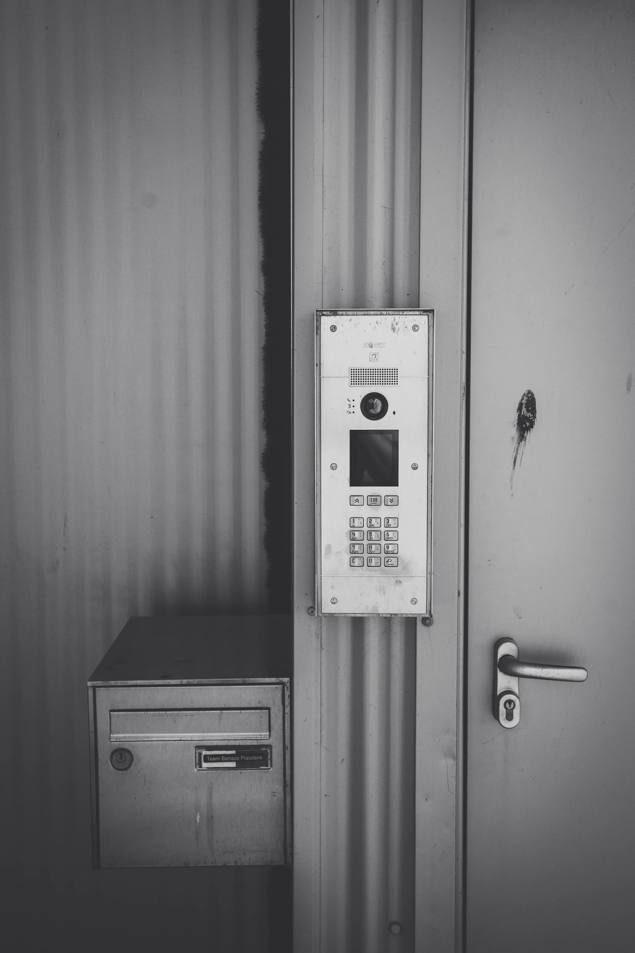 Intercom and mailbox on a corrugated metal door, black and white