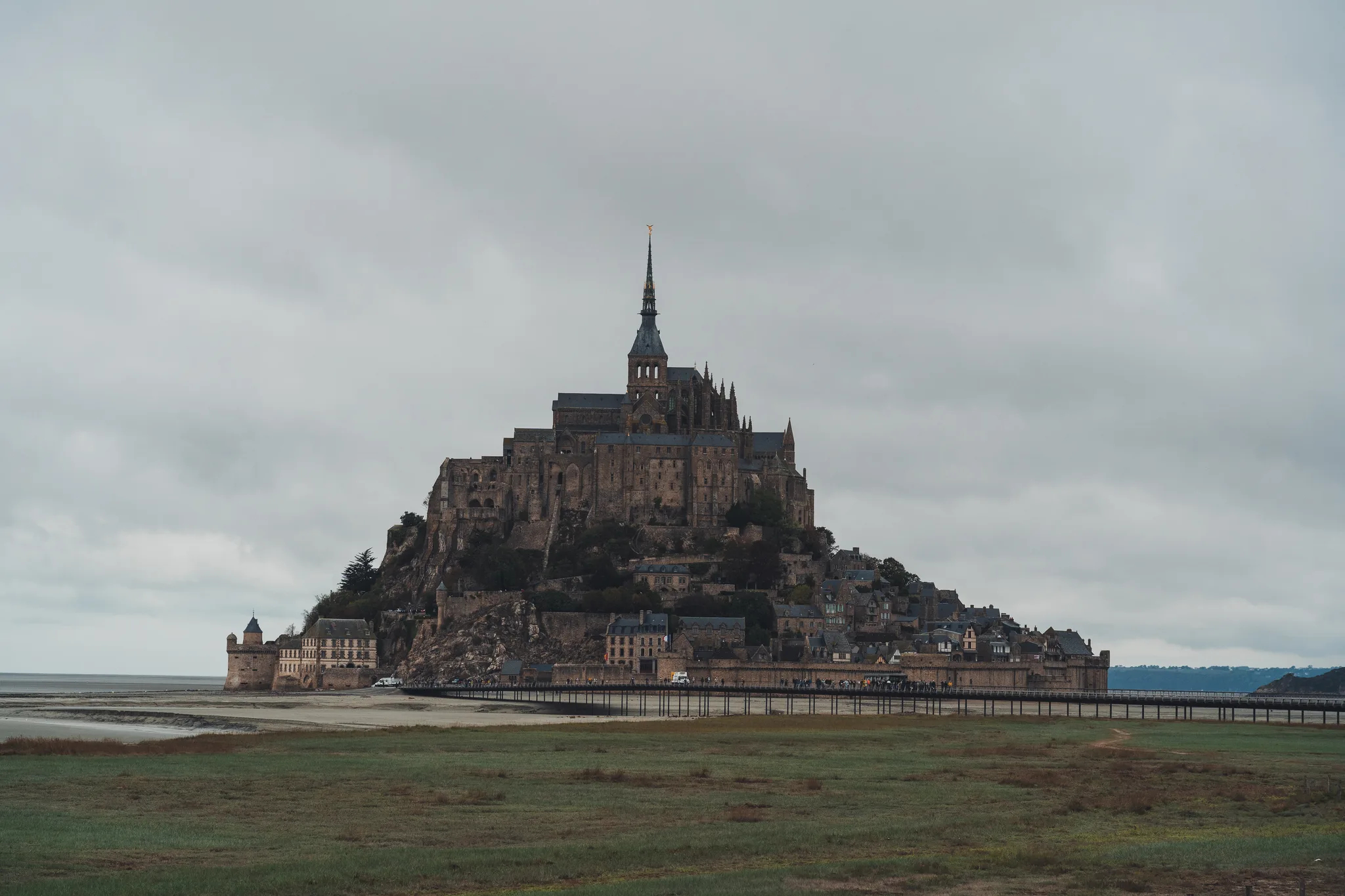 Mont-Saint-Michel and its abbey above the salt meadows under grey sky
