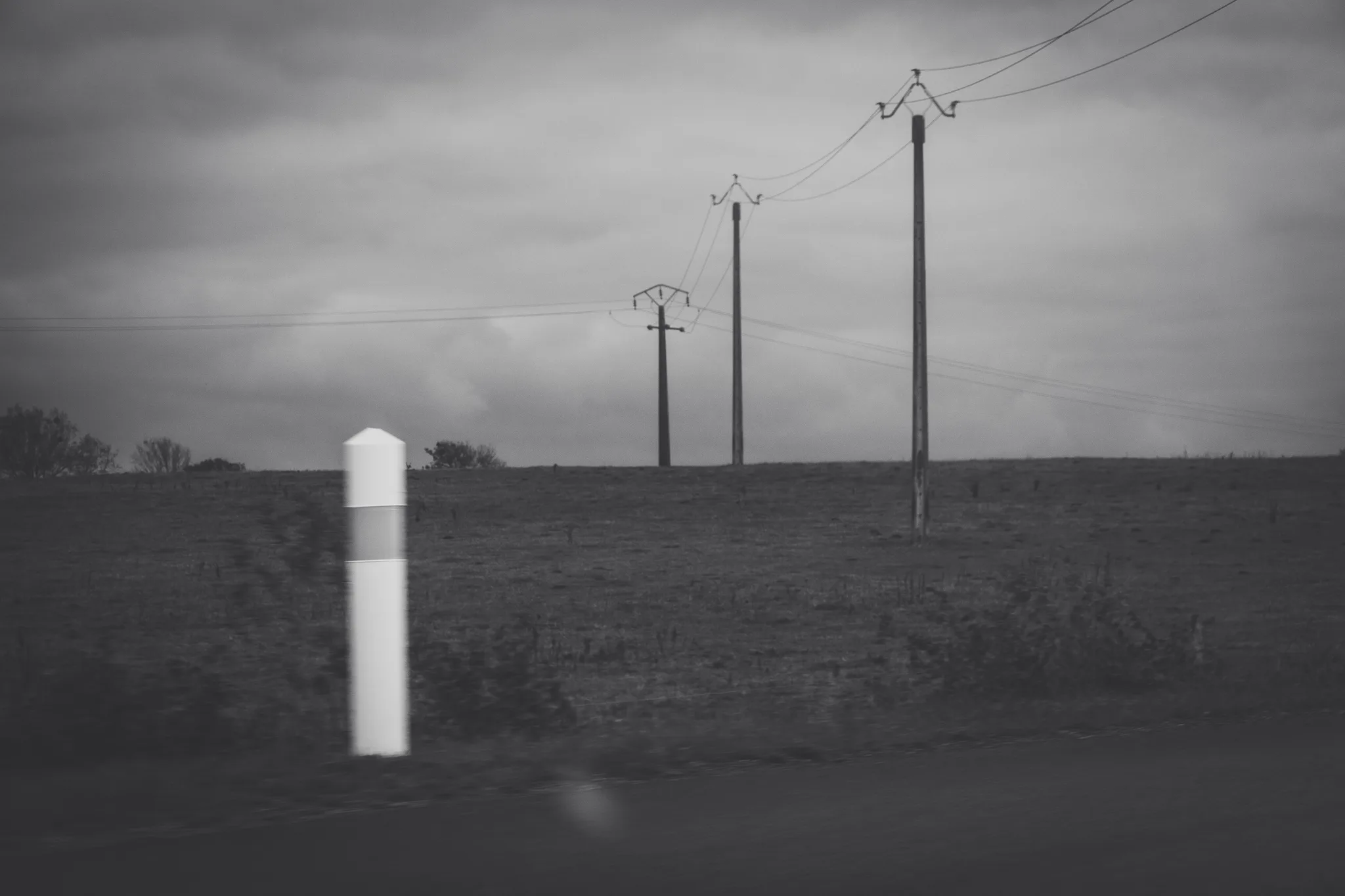 White marker post and power lines along a field, black and white
